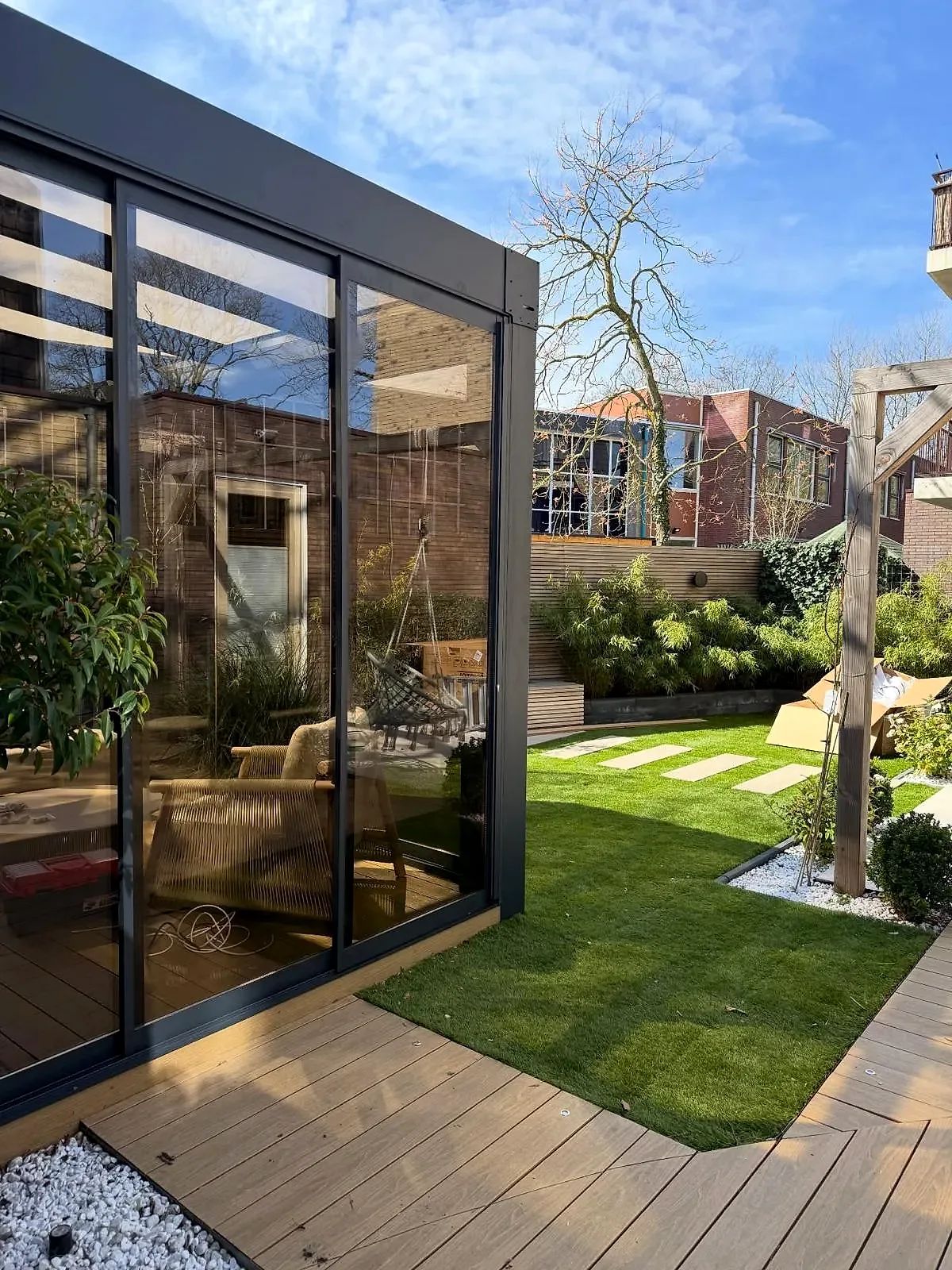 Hoek van een antraciet cube met glazen schuifwanden in een aangelegde tuin met vlonder en gras