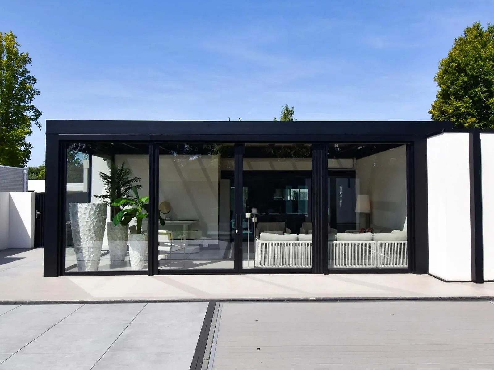 Zwarte cube met heldere glazen schuifwanden aan de voorzijde, met loungebank en planten zichtbaar door het glas