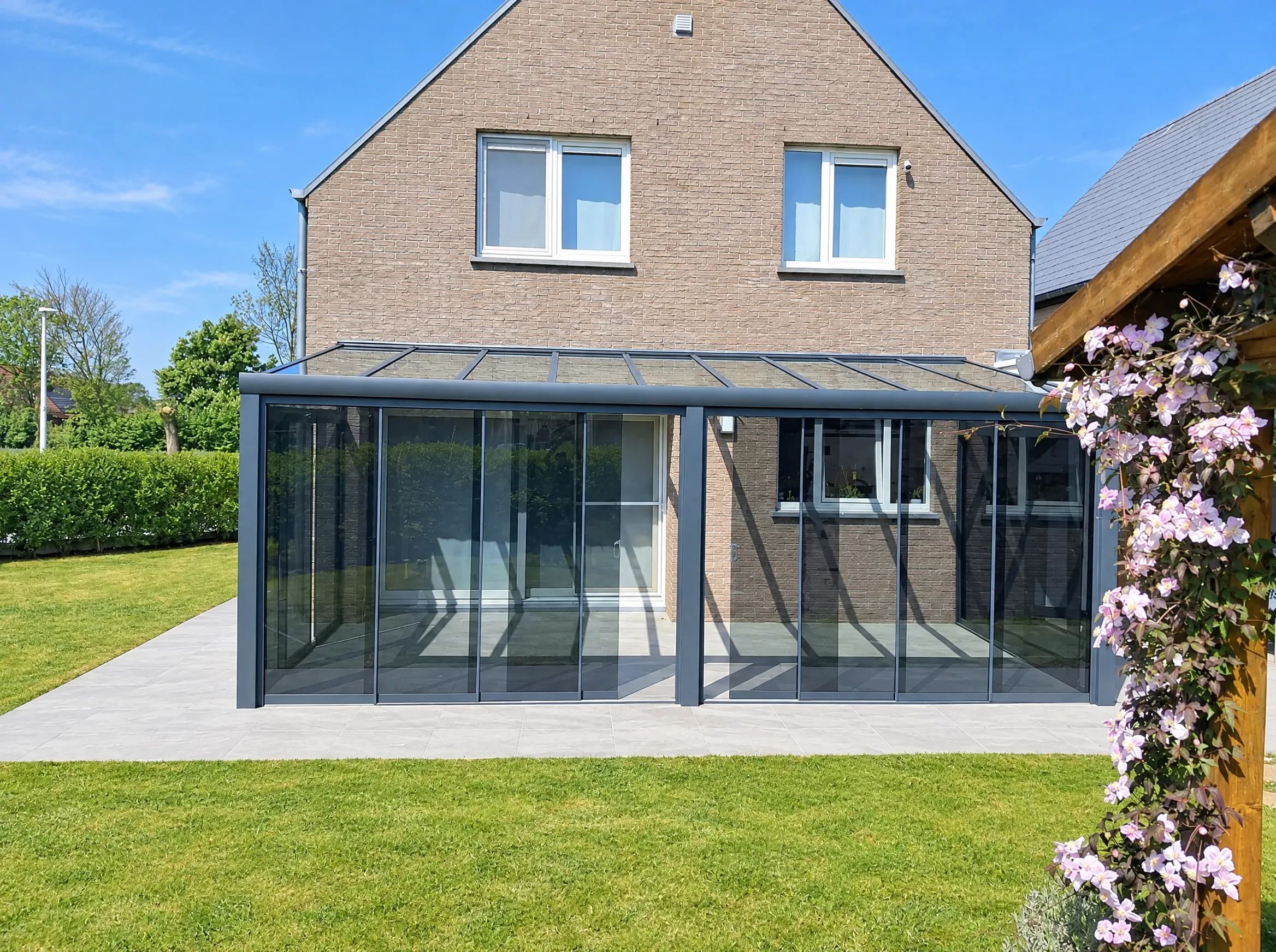 Antraciet veranda met glazen dak en getinte glazen schuifwanden aan de achterkant van een bakstenen woning